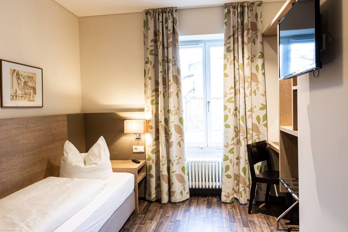 A hotel room with a bed, a desk, a chair, a TV, and curtains.