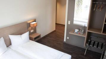 A hotel room with a bed, bedside table, lamp, and a small desk with a mirror and toiletries.