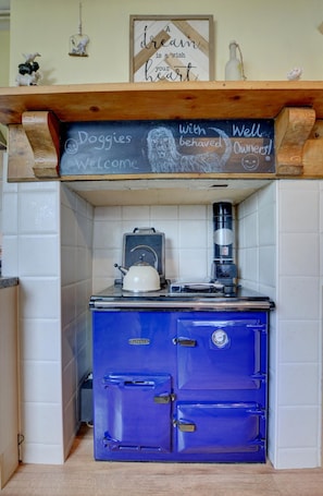 Eine Küche mit einem blauen Herd, einem Wasserkocher und einer Kaffeemaschine. Eine Tafel mit dem Text "Hunde willkommen bei angepassten Besitzern!" und ein gerahmtes Zitat befinden sich über dem Herd.