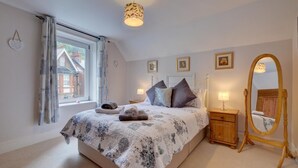 Ein Schlafzimmer mit einem großen Bett, einem Holfnachtkästchen, einem Spiegel und einem Fenster mit Vorhängen.