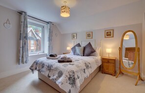 Ein Schlafzimmer mit einem großen Bett, einem Holfnachtkästchen, einem Spiegel und einem Fenster mit Vorhängen.