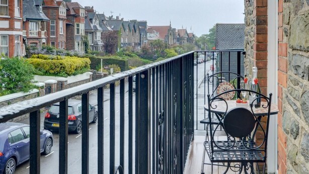 Ein Balkon mit Tisch und Stühlen, mit Blick auf eine Straße mit parkenden Autos und Häusern.