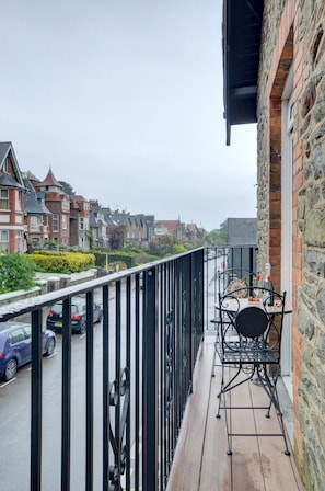 Ein Balkon mit Tisch und Stühlen, mit Blick auf eine Straße mit parkenden Autos und Häusern.