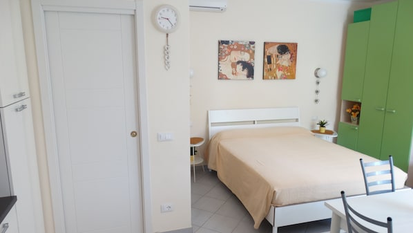 A bedroom with a bed, a bedside table, a chair, a green wardrobe, and two paintings on the wall. - ACCESSIBLE LUXURY AND SERVICES (Lerici)