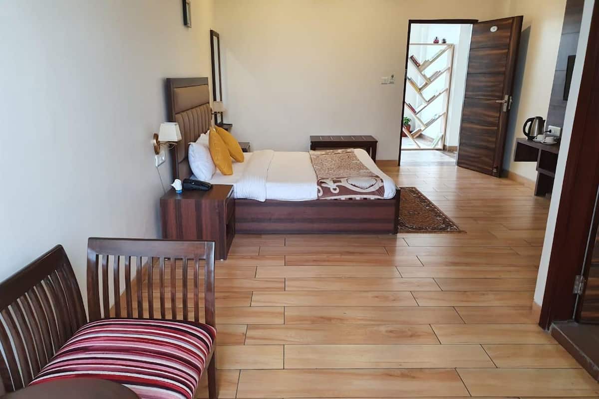 A hotel room with a bed, a wooden bench, a small table, and a bookshelf.
