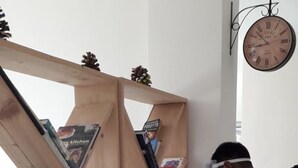 A wooden bookshelf filled with books, a wall clock, and a person in white protective clothing. - Serene Suites (Dharamshala)