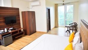 A hotel room with a bed, a TV, a wardrobe, a desk, and a balcony with a chair. - Serene Suites (Dharamshala)