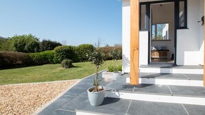 A modern house with a stone patio, potted plants, and a view of the surrounding landscape. - 5 Bed in Croyde (oc-fircon) (Croyde)