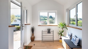 A room with a wooden floor, a window with a view of greenery, a plant, and a bench. - 5 Bed in Croyde (oc-fircon) (Croyde)
