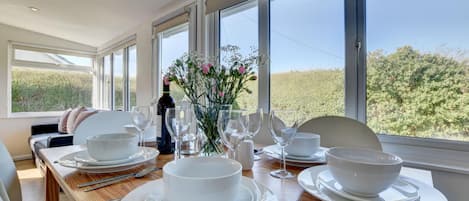 A dining area with a table set for four, large windows, and a view of greenery outside.