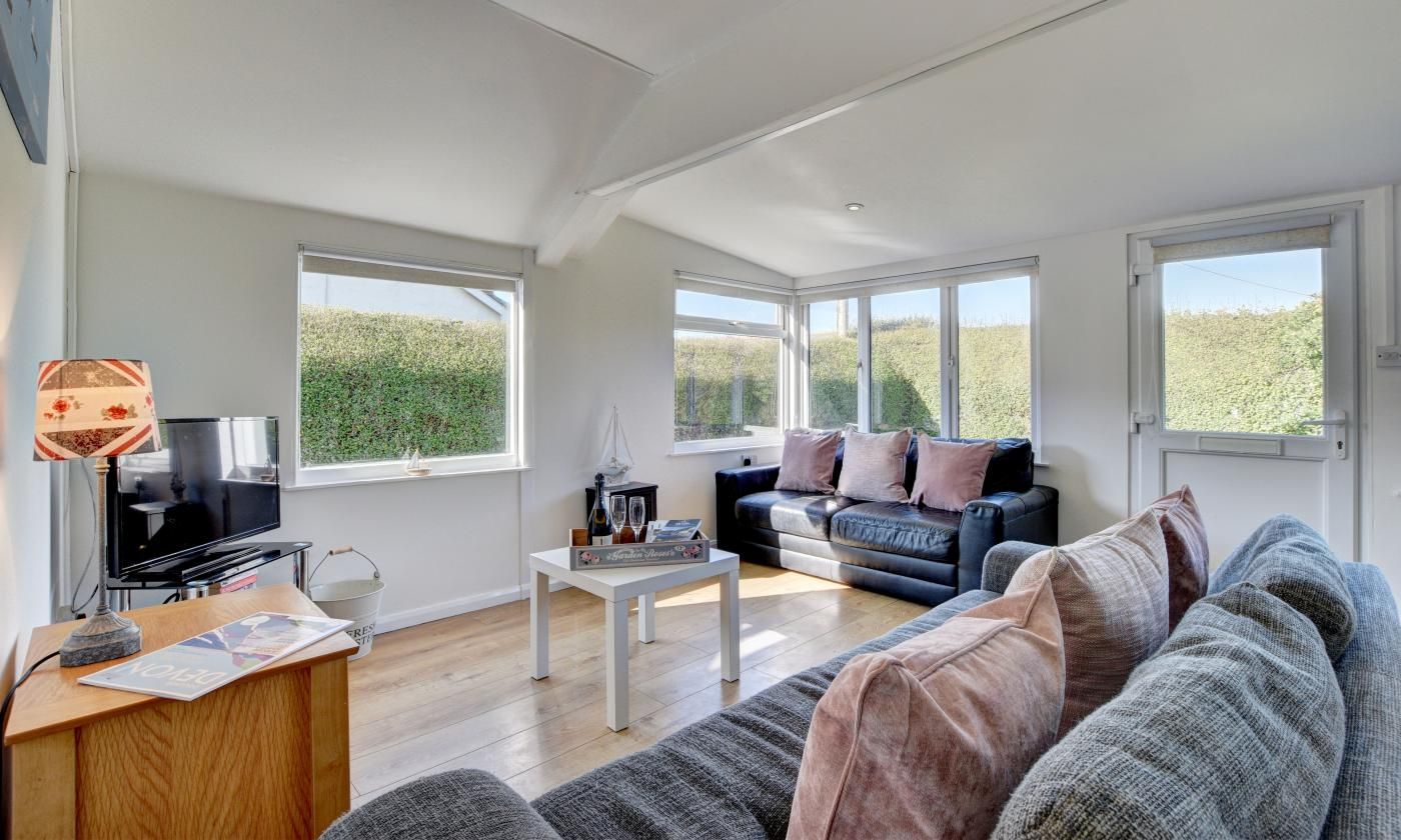 A spacious living room with a large window, a black sofa, a white coffee table, and a television on a wooden stand.