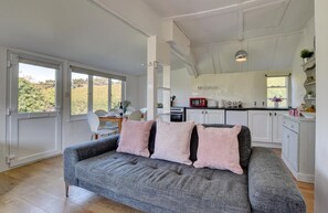 A cozy living room with a grey sofa, a dining area with a table and chairs, and a kitchen with white cabinets and appliances.