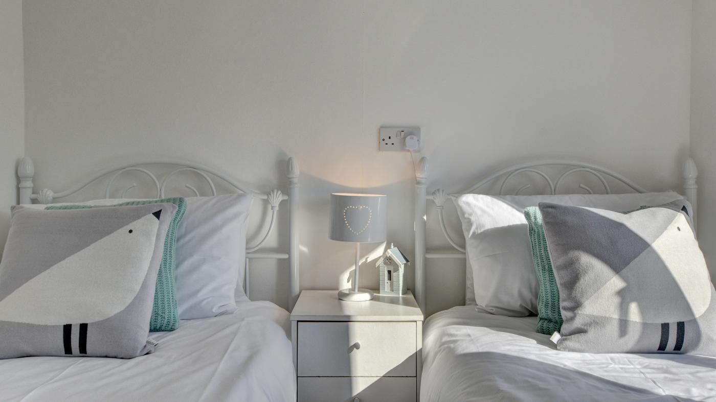 A twin bedroom with white beds, matching nightstands, and a bedside table with a lamp.