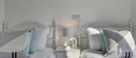 A twin bedroom with white beds, matching nightstands, and a bedside table with a lamp.
