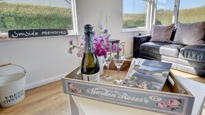 A cozy living room with a view of the countryside, a bottle of wine, and a tray of oysters. - 3 Bed in Croyde (oc-moonra) (Croyde)
