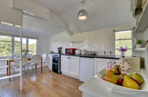 Een lichte keuken met witte kastjes, een houten eettafel en een fruitschaal.