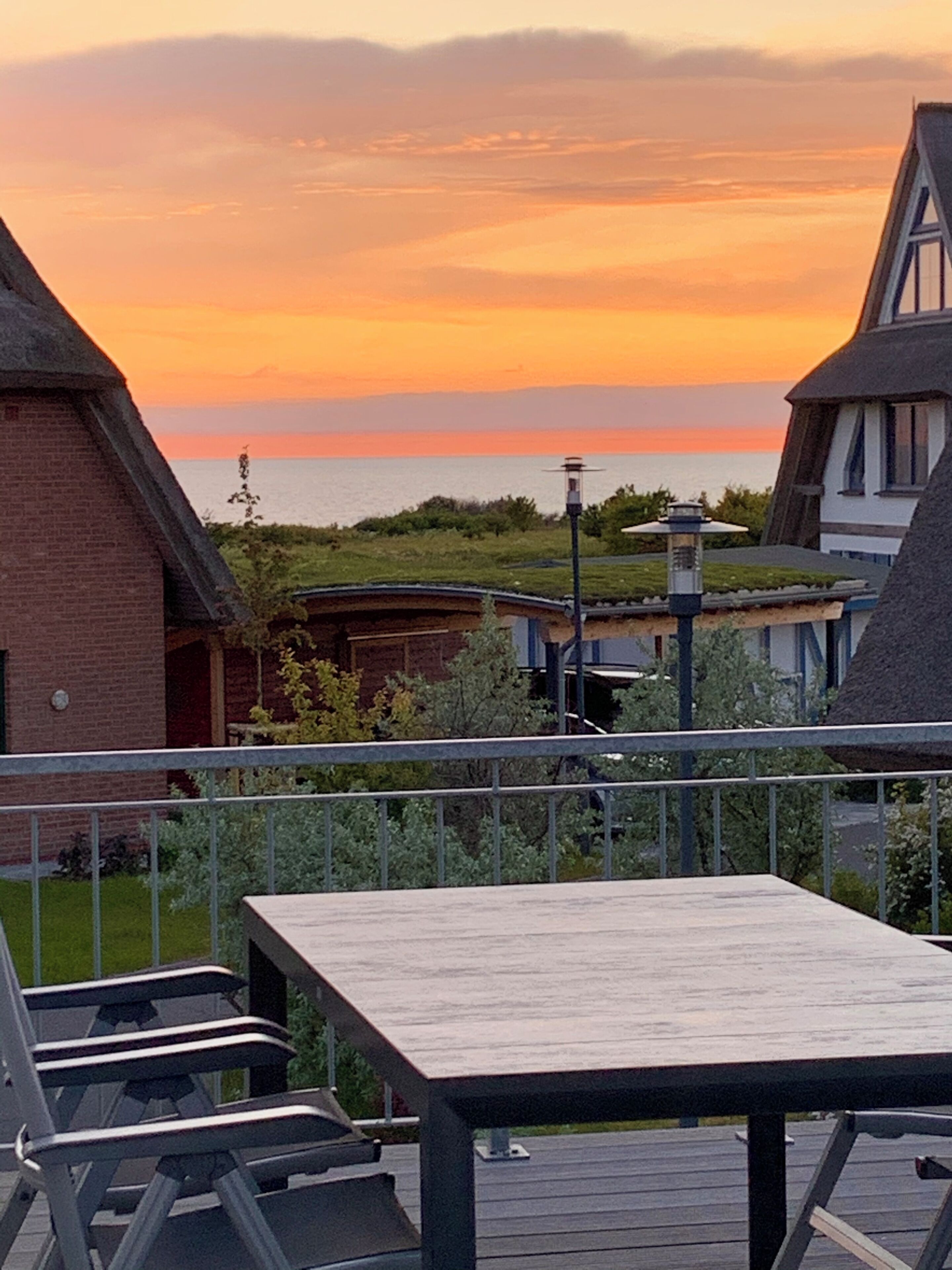 Una terraza con vista al atardecer sobre el mar, un edificio de ladrillo y un farol.