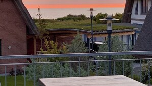 En terrasse med udsigt til solnedgangen over havet, en murstensbygning og en lygtepæl.