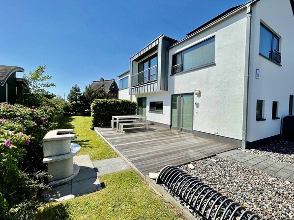 Una casa moderna de dos pisos con una terraza de madera, un macetero de piedra y un camino de grava.
