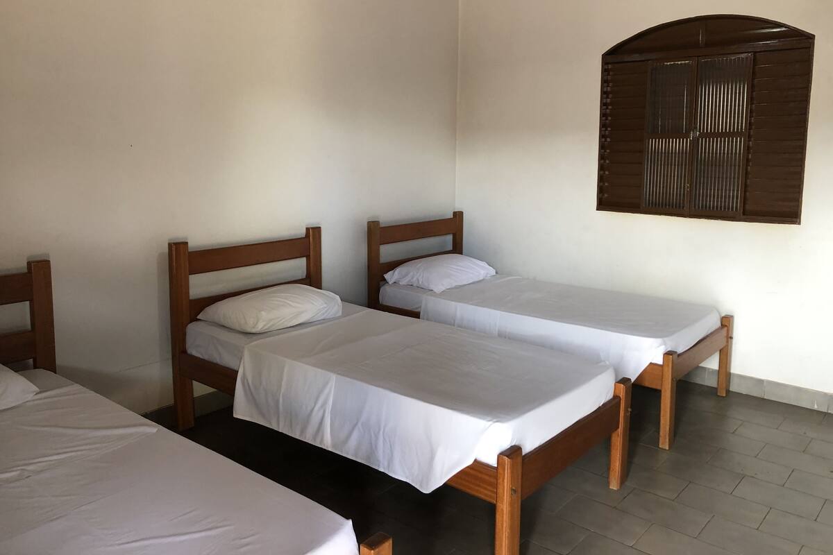 Habitación con tres camas de madera alineadas a la pared, cada una con ropa blanca.