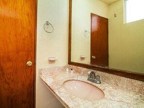 Un baño con puerta de madera, lavamanos de mármol, espejo y argolla para toallas en la pared.