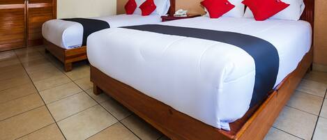 A hotel room with two wooden beds, each with white bedding and red pillows.