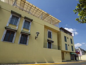 Un edificio amarillo con varias ventanas, un balcón y un letrero que indica un hotel.