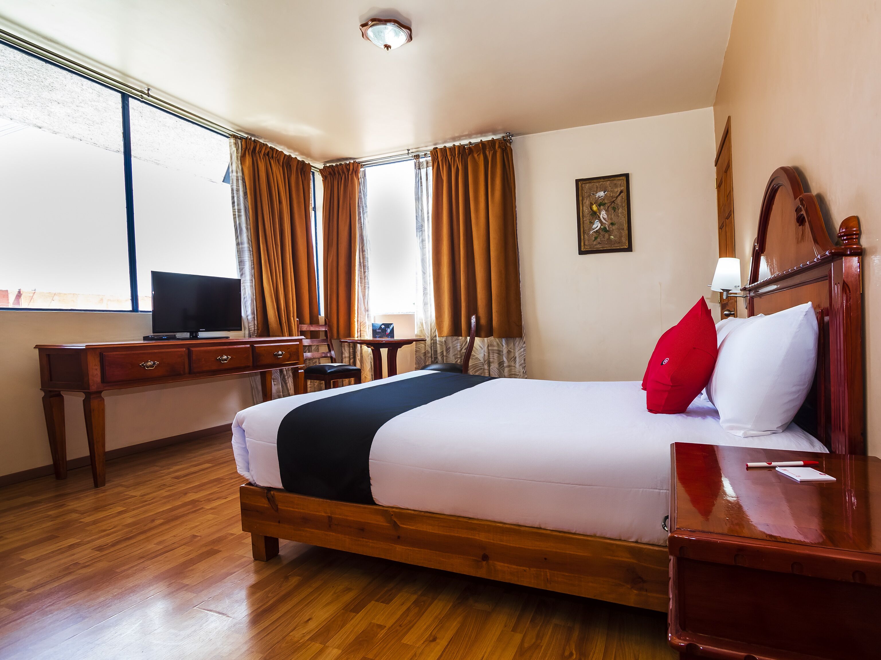 A hotel room with a large bed, wooden furniture, a desk, and a television.
