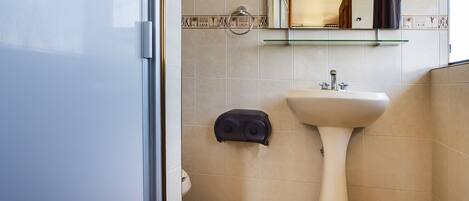 A bathroom with a white sink, a mirror above it, and a glass shelf.