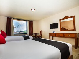 Habitación de hotel con dos camas, un escritorio, una silla, un televisor y un ventanal con vistas.
