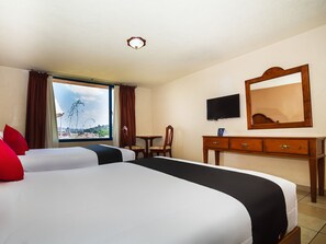 Habitación de hotel con dos camas, un escritorio, una silla, un televisor y un ventanal con vistas.
