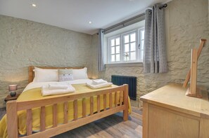 A bedroom with a wooden bed, a bedside table, a mirror, and a window with curtains. - 2 Bed in Appledore (oc-hide1) (Appledore)