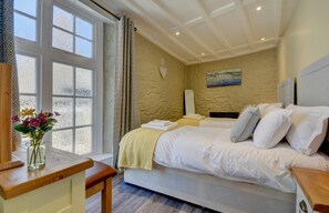Une chambre à coucher avec un lit, une table de chevet, une chaise, une fenêtre et un tableau au mur.