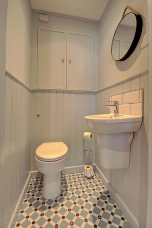 A bathroom with a toilet, sink, and mirror. - 2 Bed in Appledore (oc-hide1) (Appledore)