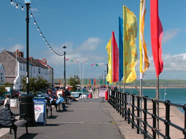 Une promenade en bord de mer, bordée d’une rangée de drapeaux, de bancs et d’un panneau indiquant le nom du journal « Western Morning News ».