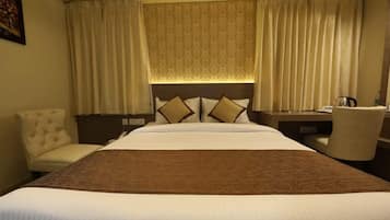 Una habitación de hotel con una cama grande, un cabecero con almohadones decorativos, un escritorio con una silla y cortinas.