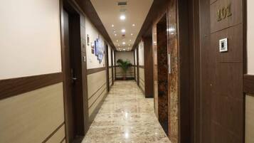 Un pasillo de hotel con piso de mármol, puertas de madera y una planta en maceta.