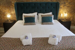 A neatly made bed with a teal headboard, white linens, and patterned pillows. There are two bedside tables with lamps and towels on the bed. - Art'otel Barcelos (Barcelos)