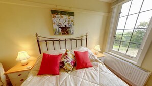 Een slaapkamer met een bed, twee nachtkastjes, een raam en een schilderij aan de muur.