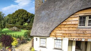 Een traditioneel rieten huis met een verzorgde tuin en een helder uitzicht op het omliggende landschap.