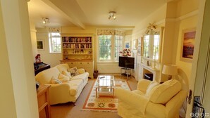 A cozy living room with a sofa, armchair, and a fireplace. There is a bookshelf filled with books and a television in the corner. - Rock House Cottage (Exeter)
