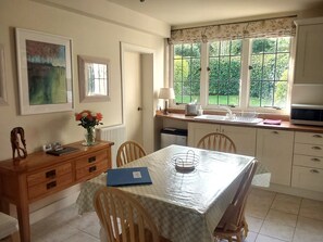 Un comedor con una mesa lista para cuatro personas, una ventana con vistas a zonas verdes y una cocina con microondas y fregadero.