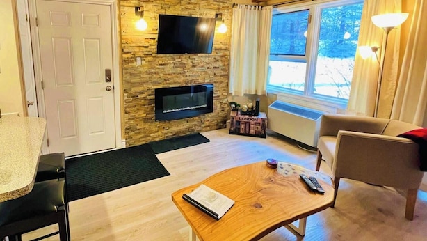 A cozy living room with a stone wall, a flat-screen TV, a wooden coffee table, and a sofa. - Rustic Mountainside Chalet (The Blue Mountains)