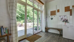 A room with a large sliding glass door leading to an outdoor area, a small bench, a refrigerator, and a wall-mounted heart-shaped decoration. - 3 Bed in Parracombe (oc-molec) (Parracombe)