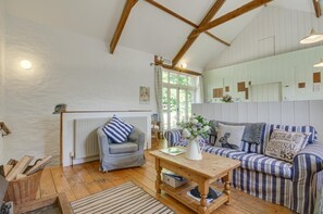 Une piÚce chaleureuse avec un plancher en bois, un canapé à rayures, un fauteuil, une table avec un vase et un radiateur.
