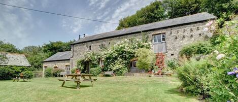 A stone building with a garden, picnic table, and a stone wall.