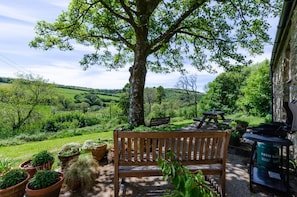 A bench, a picnic table, and potted plants in a garden with a view of a green landscape.