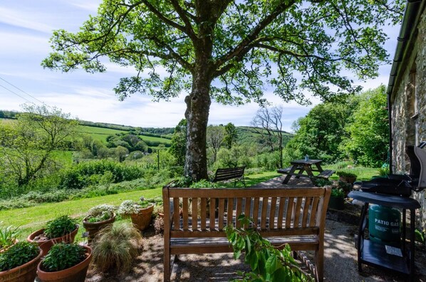 A bench, a picnic table, and potted plants in a garden with a view of a green landscape.
