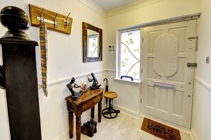 A hallway with a coat rack, a mirror, a door with a window, and a wooden table with decorative items. - Canning Town House (London)