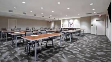 A conference room with multiple tables and chairs, a carpeted floor, and ceiling lights.